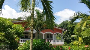 A house with a red roof and white walls, surrounded by lush greenery and a clear blue sky. - Polish Princess Guest House (Port Antonio)