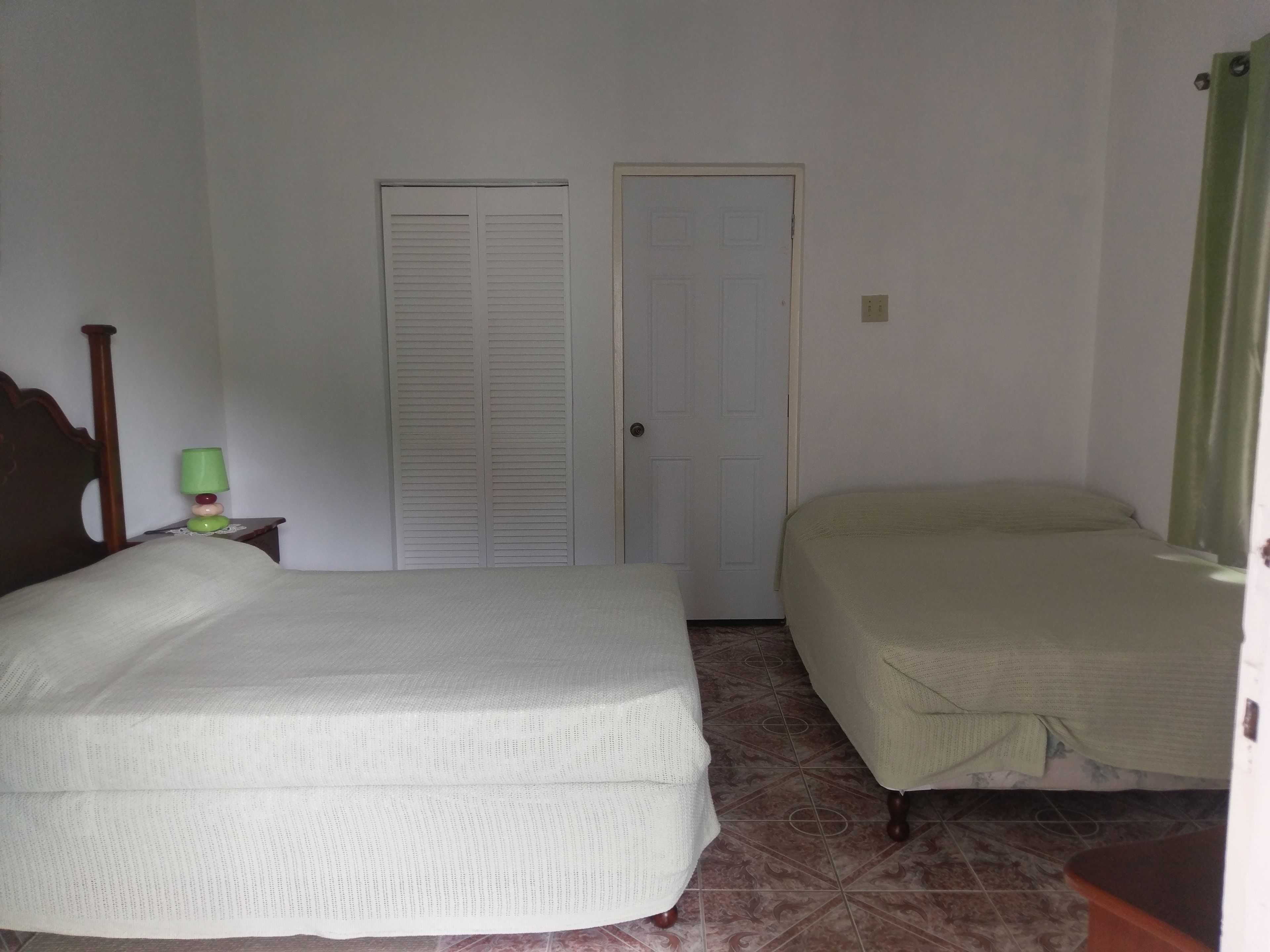 Un dormitorio con dos camas, cabecero de madera, mesita de noche con lámpara y una puerta.