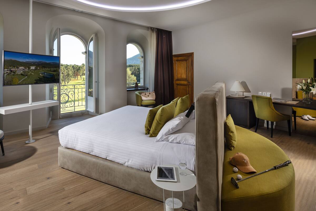 Une chambre d’hôtel moderne, dotée d’un grand lit, d’un bureau, d’une chaise et d’un téléviseur diffusant des images d’un paysage magnifique.