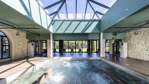 Un área de piscina interior espaciosa con tragaluces, paredes de piedra e iluminación moderna.