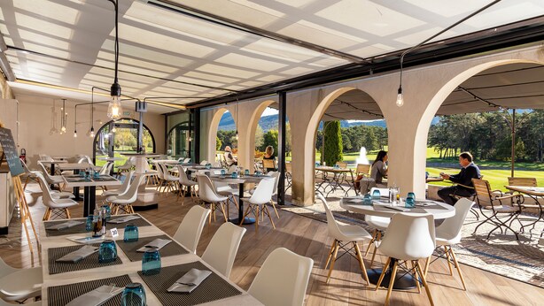 Un restaurante con terraza, mesas dispuestas con vajilla y vistas a un campo de golf.