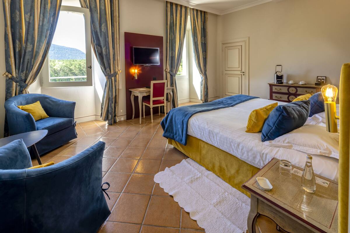 Une chambre d’hôtel avec un lit, un bureau, une chaise, une télévision et une fenêtre avec des rideaux.