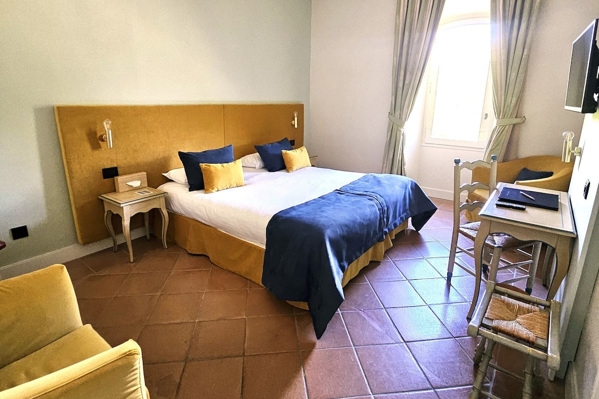 Une chambre d’hôtel avec un lit, un bureau, une chaise et une fenêtre avec des rideaux.