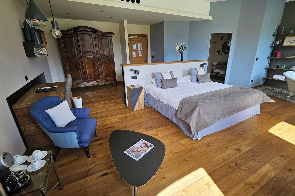 Une chambre à coucher moderne avec un grand lit, un fauteuil bleu, une petite table et une armoire en bois.