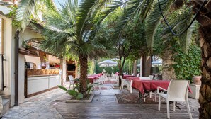 An outdoor dining area with stone flooring, white wicker chairs, and red tablecloths. - Corte Cristina (Quartucciu)