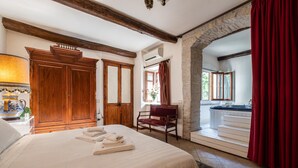 A hotel room with a large bed, wooden wardrobe, a red chair, and a view of the outside through a window. - Corte Cristina (Quartucciu)