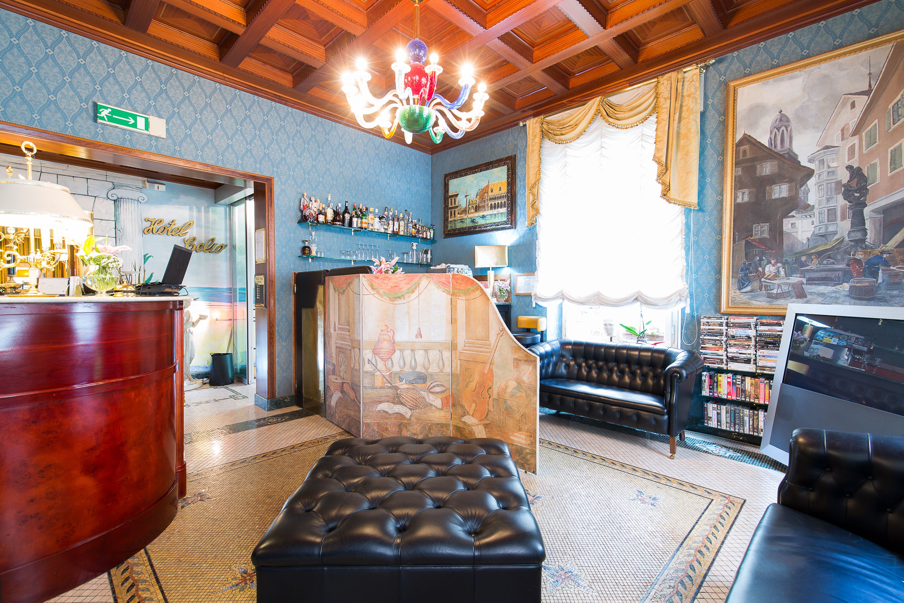 Un vestíbul amb zona de bar, un llum elegant i gran, una zona d'estar amb un sofà i otomana, i una biblioteca plena de llibres.