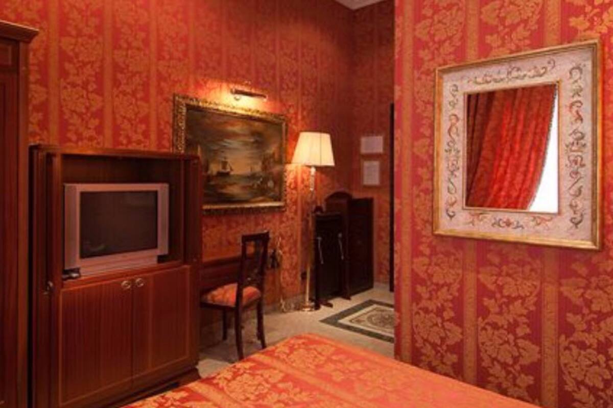 Ein Hotelzimmer mit Holzschrank, Fernseher, Schreibtisch mit Stuhl, Lampe und einem gerahmten Bild an der Wand.