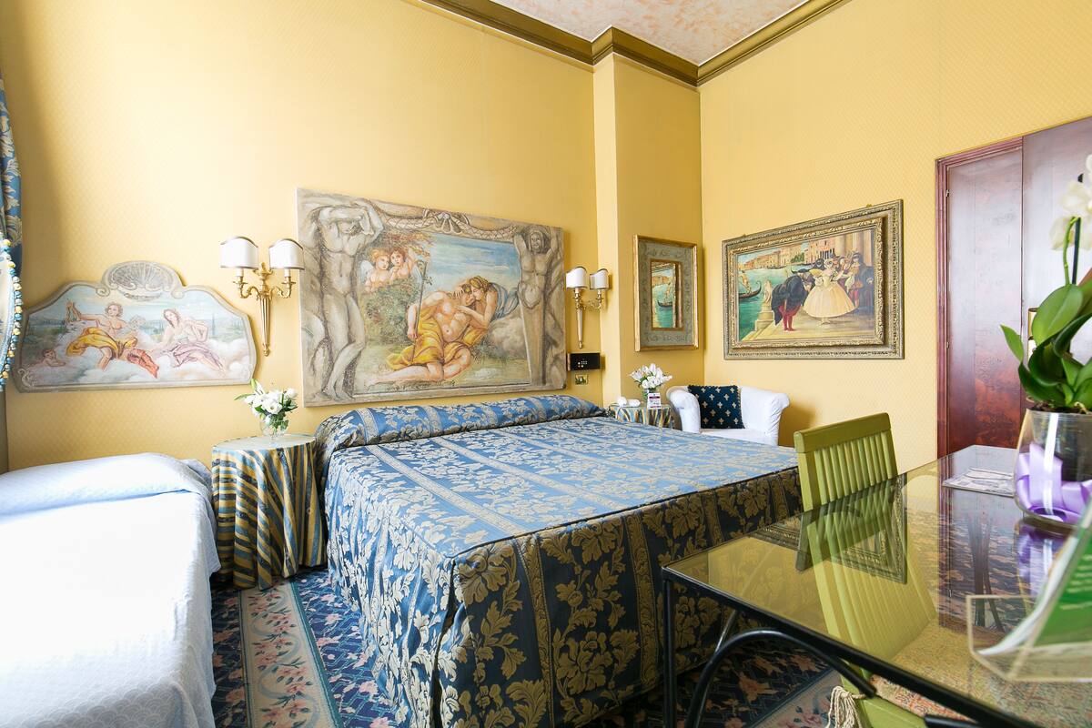 Ein Hotelzimmer mit Bett, Esstisch mit Stühlen, einem kleinen Beistelltisch und einem Bild an der Wand.