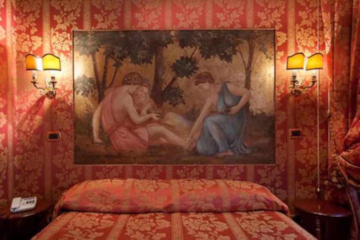 Ein Hotelzimmer mit einem großen, klassischen Gemälde an der Wand, einer gemusterten Bettdecke und zwei Wandleuchten.