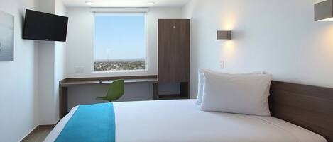 A hotel room with a bed, a desk, a chair, a TV, and a window with a city view.