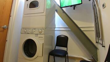 A laundry room with a washing machine, a chair, and a TV mounted on the wall.
