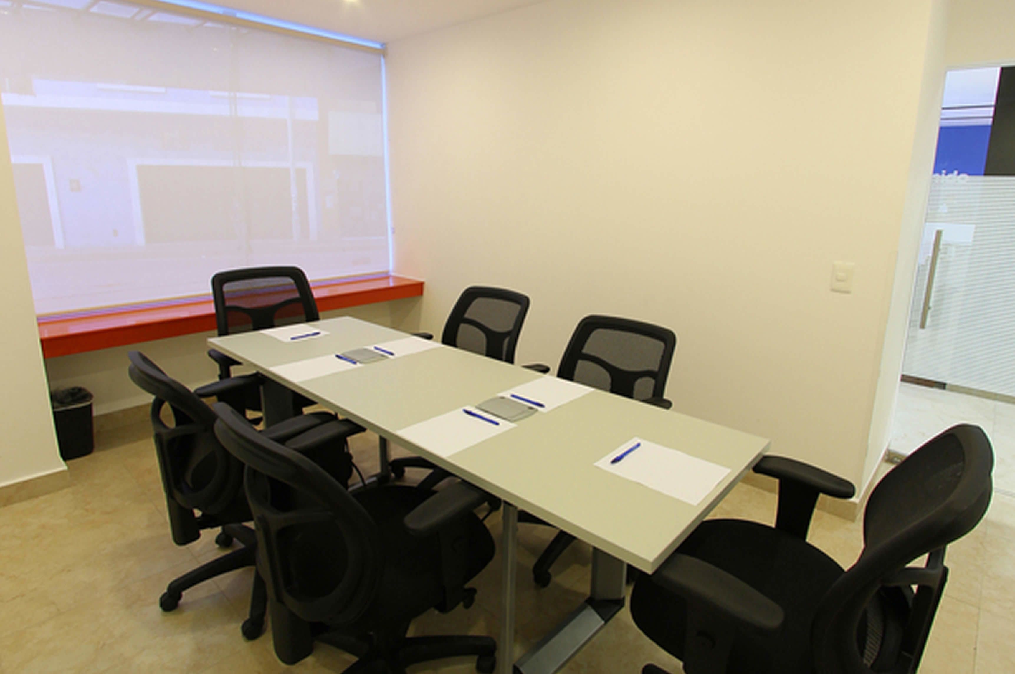 Una sala de conferencias con una larga mesa, seis sillas y una pantalla para proyector.