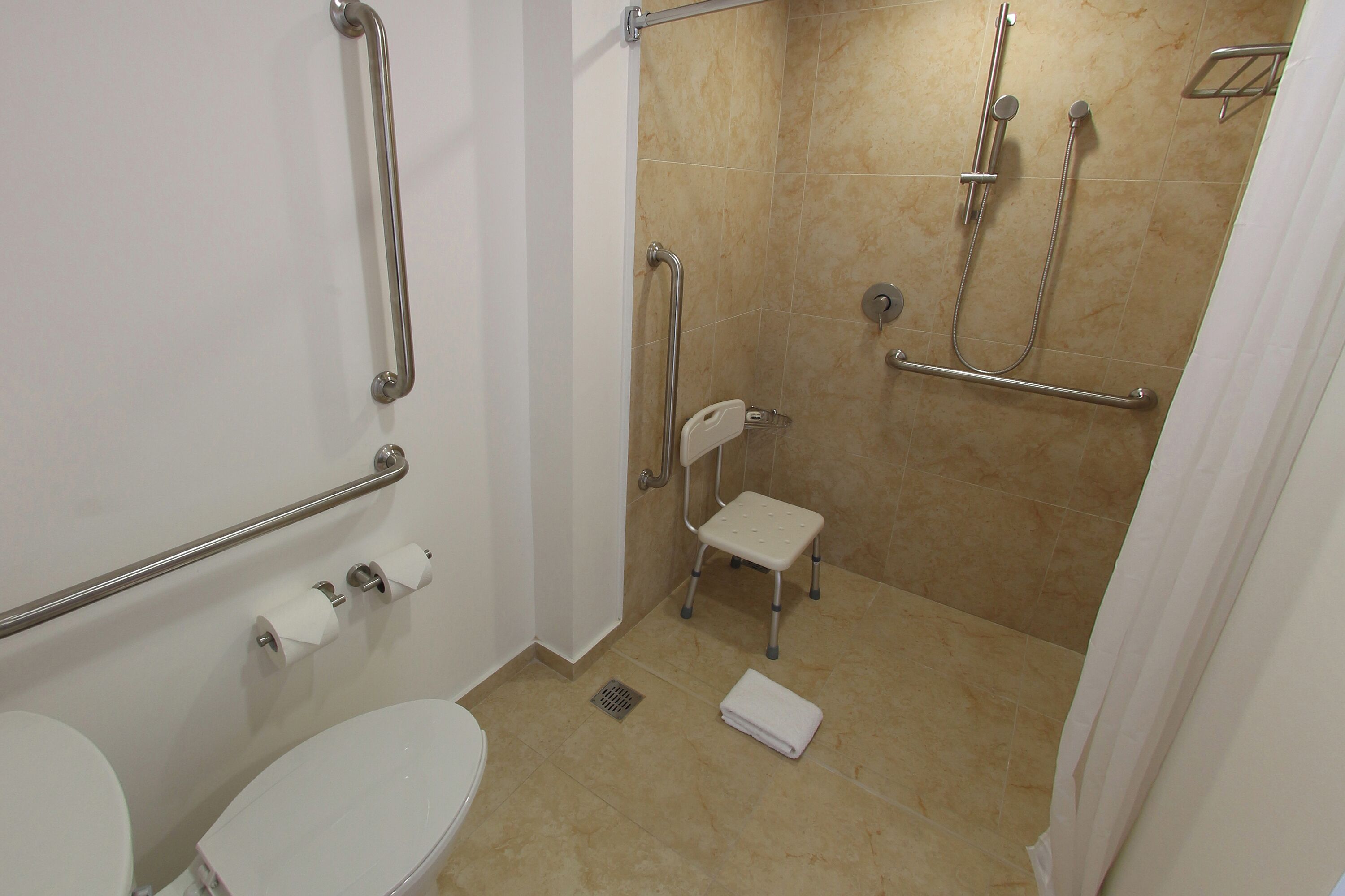 Une salle de bain équipée de toilettes, de barres d’appui, d’une douche avec un pommeau de douche amovible et d’un marchepied.