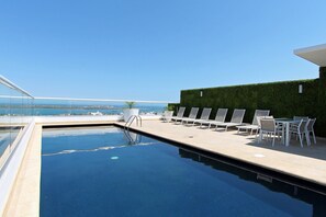 A rooftop pool with clear blue water, surrounded by white lounge chairs and a table. - One La Paz Hotel (La Paz)
