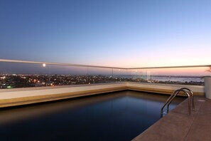 A rooftop pool with a glass railing, offering a city view at dusk. - One La Paz Hotel (La Paz)