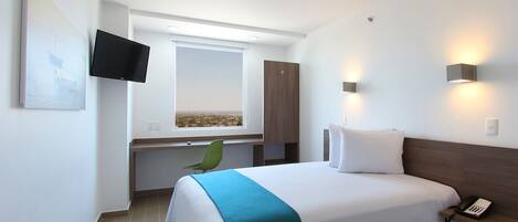 A hotel room with a bed, a desk, a chair, a TV, and a window with a city view.