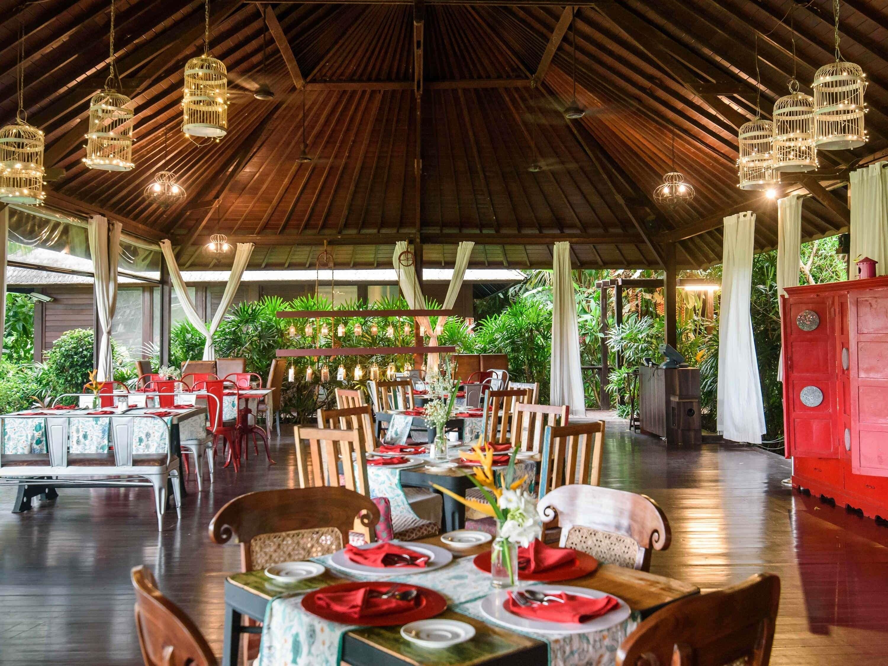 Un comedor interior con mesas y sillas de madera, y lámparas colgantes.