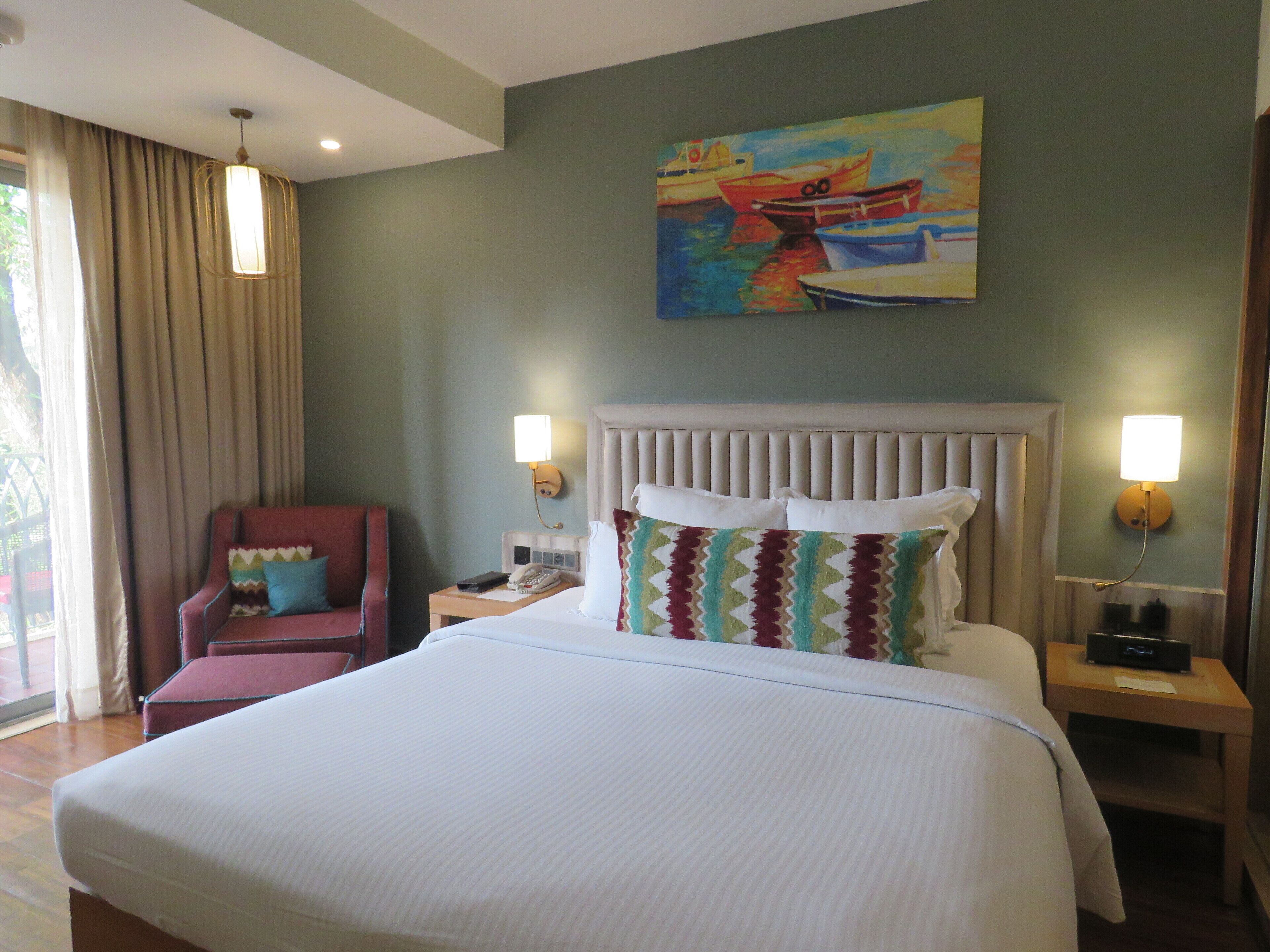 Ein Hotelzimmer mit einem großen Bett, einem roten Sessel, einem Bild von Booten an der Wand und zwei Nachttischlampen.