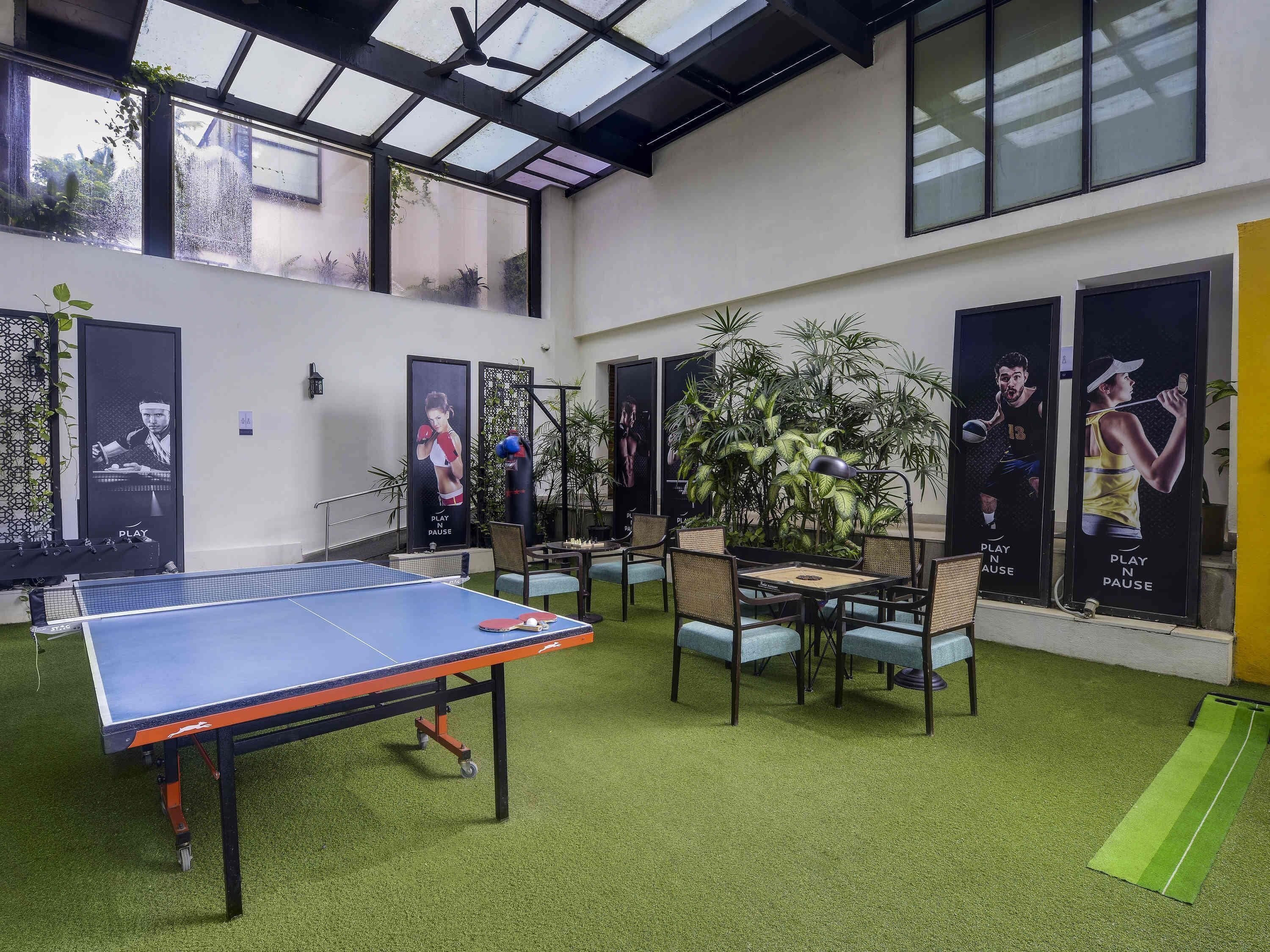 A ping pong table, chairs, and posters in a room with a high ceiling and large windows.
