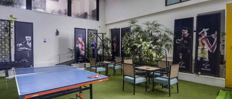 A ping pong table, chairs, and posters in a room with a high ceiling and large windows.