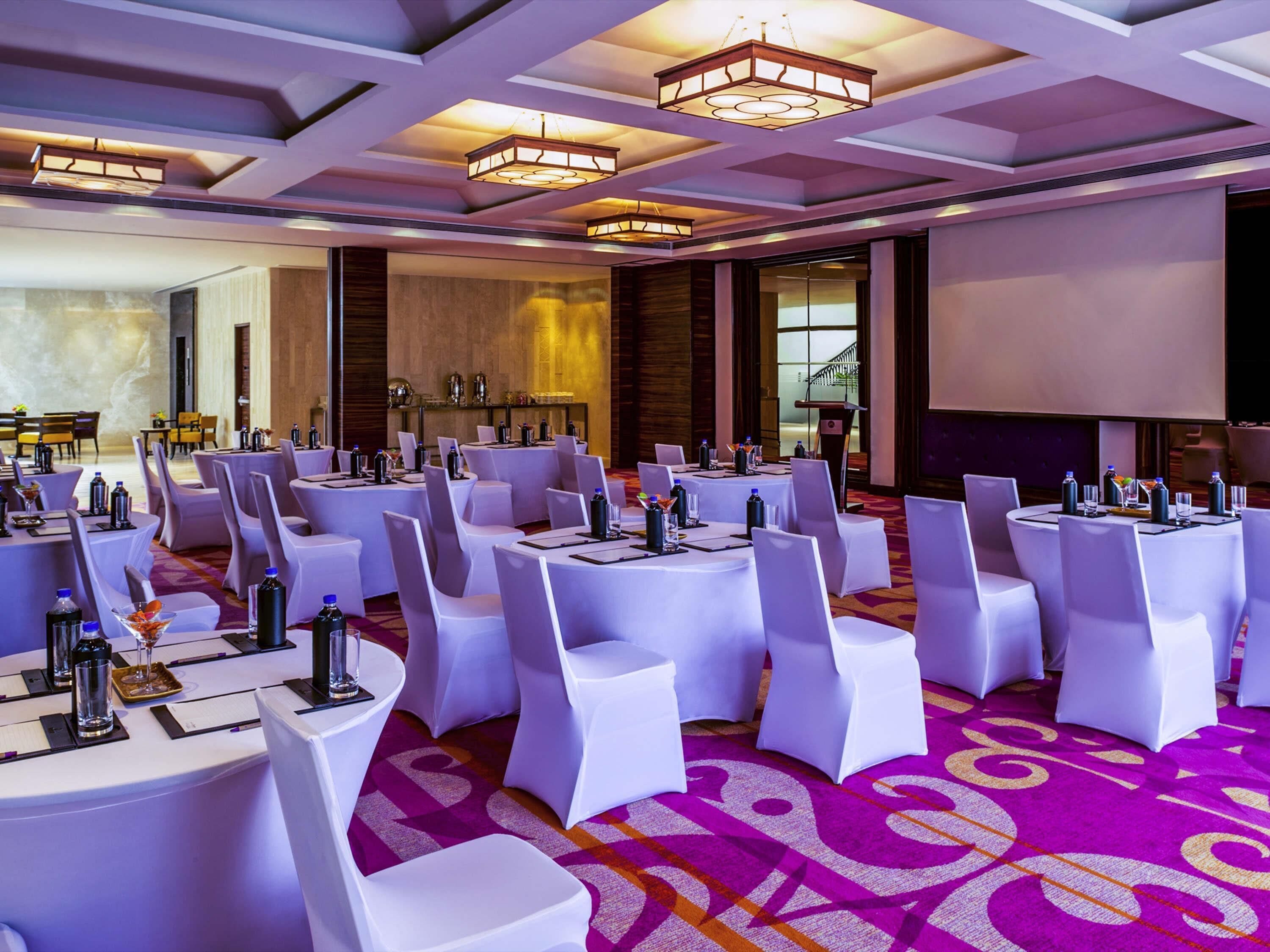 A conference room with round tables, white chairs, and a carpeted floor.