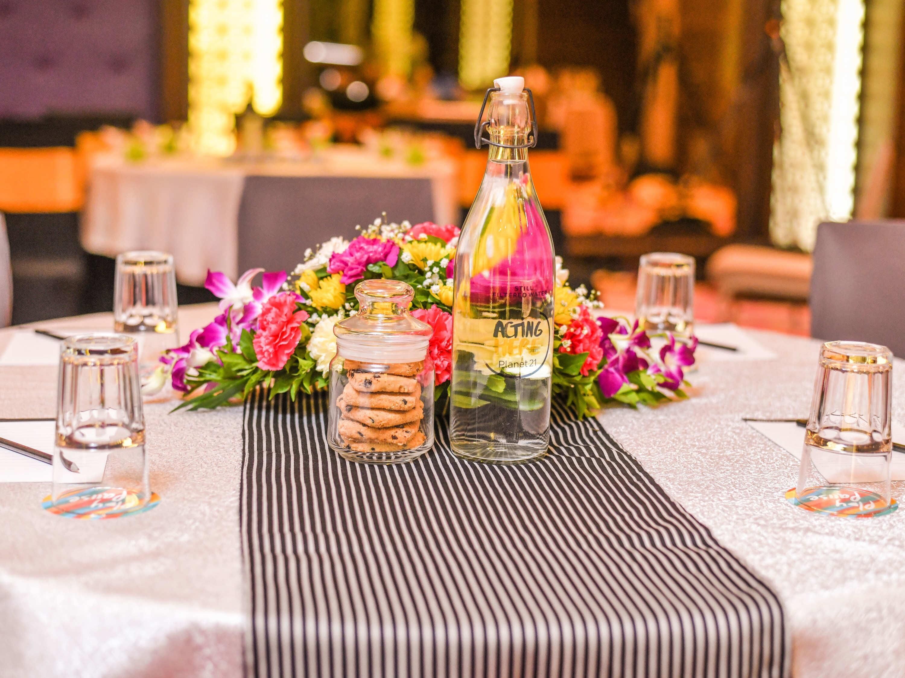A table set with a glass bottle, a jar of cookies, and a floral arrangement.