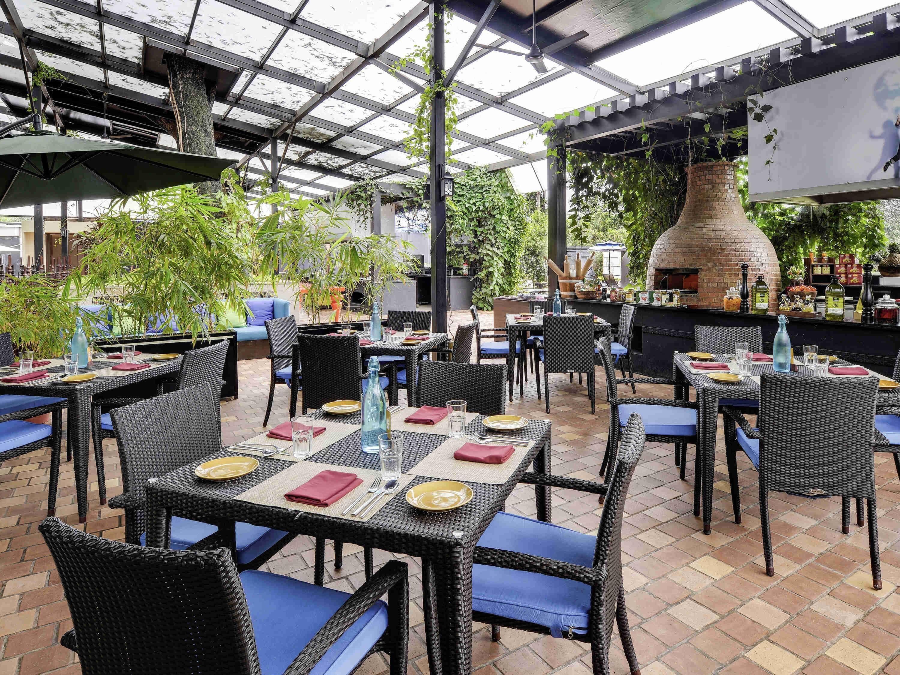 Un espace extérieur aménagé pour les repas, avec des tables et des chaises, un four en briques et de la verdure.