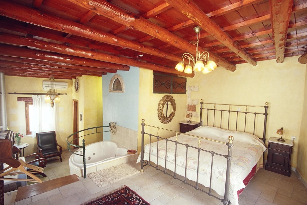 A bedroom with a large bed, a wooden ceiling, a bathtub, and a chandelier.