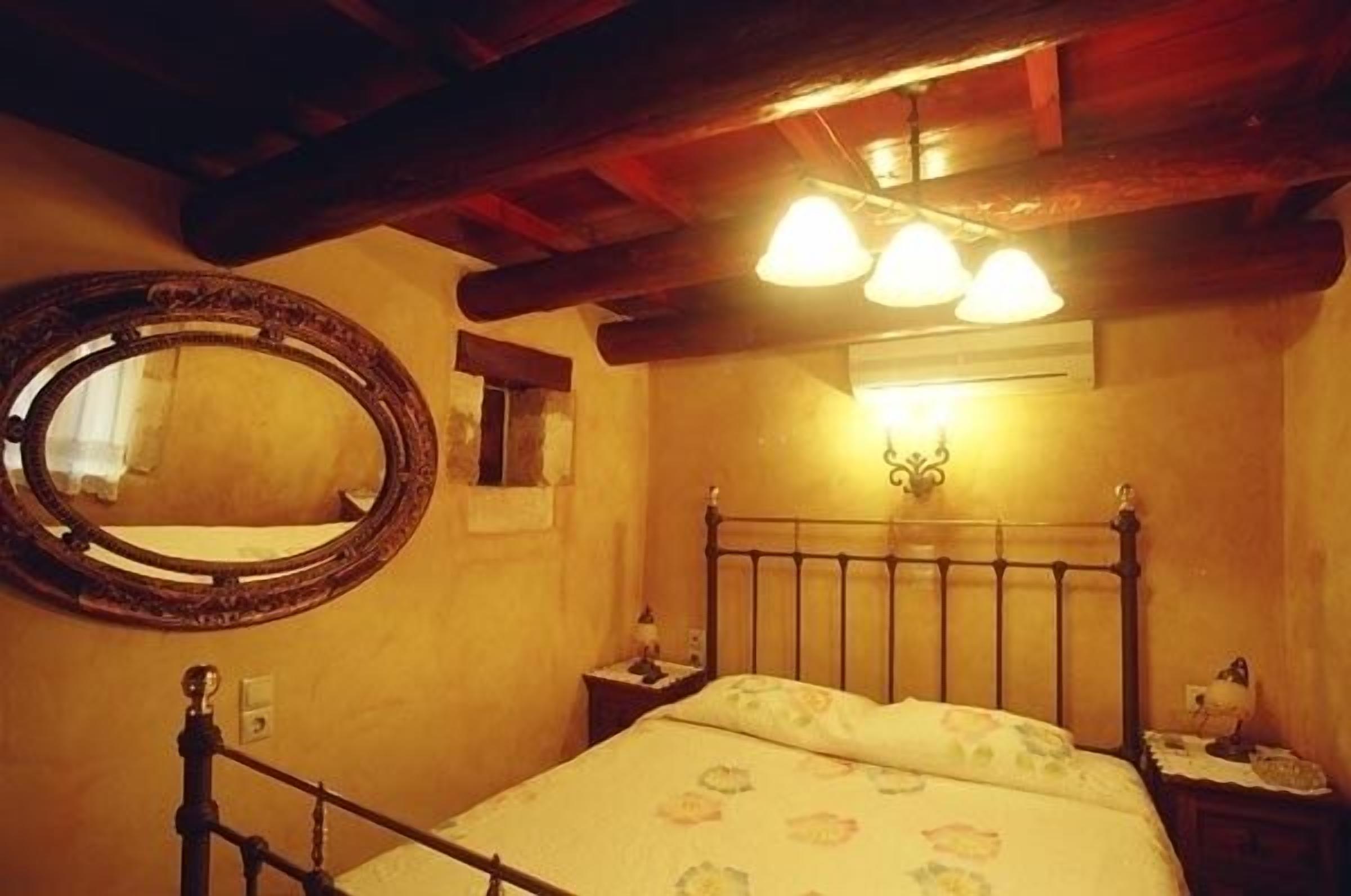 A bedroom with a wooden bed frame, a round mirror, and a wall-mounted light fixture.