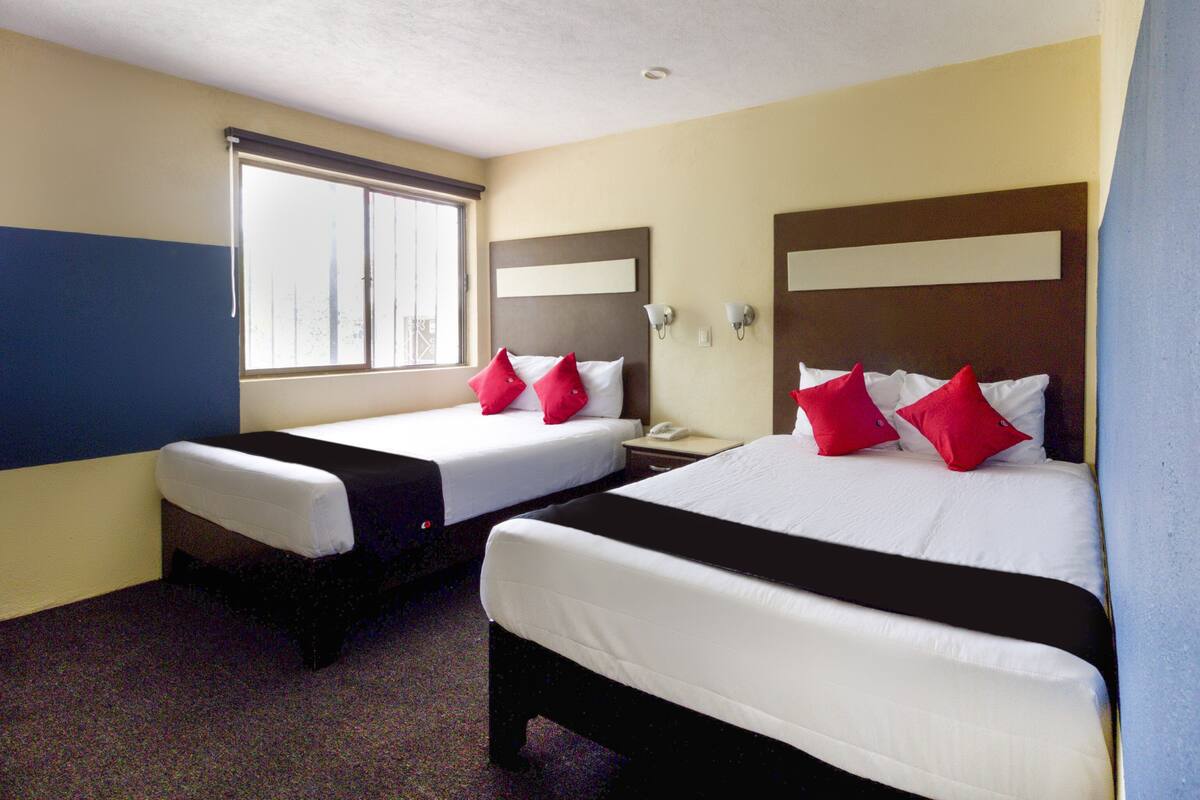 A hotel room with two beds, a window, and a nightstand with a phone.