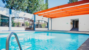 A swimming pool with a metal ladder, surrounded by a white building with large windows and an orange roof structure. - Hotel La Fuente, Saltillo (Saltillo)