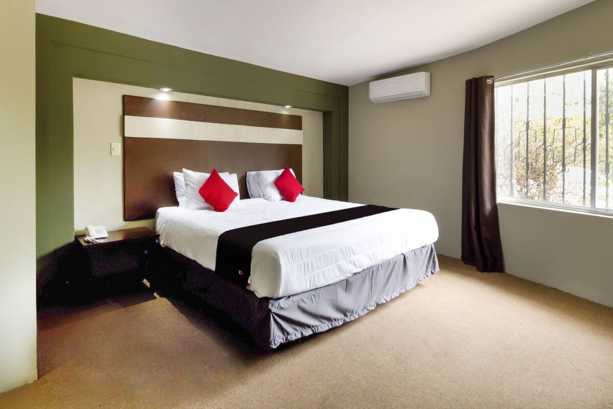 A hotel room with a large bed, a telephone, an air conditioning unit, and a window with curtains.
