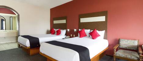 A hotel room with two beds, a wooden headboard, a red accent wall, and a single chair.