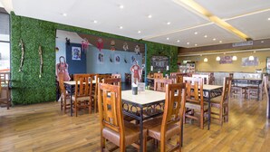 A restaurant with wooden tables and chairs, a green wall with decorations, and a ceiling with recessed lighting. - Hotel La Fuente, Saltillo (Saltillo)