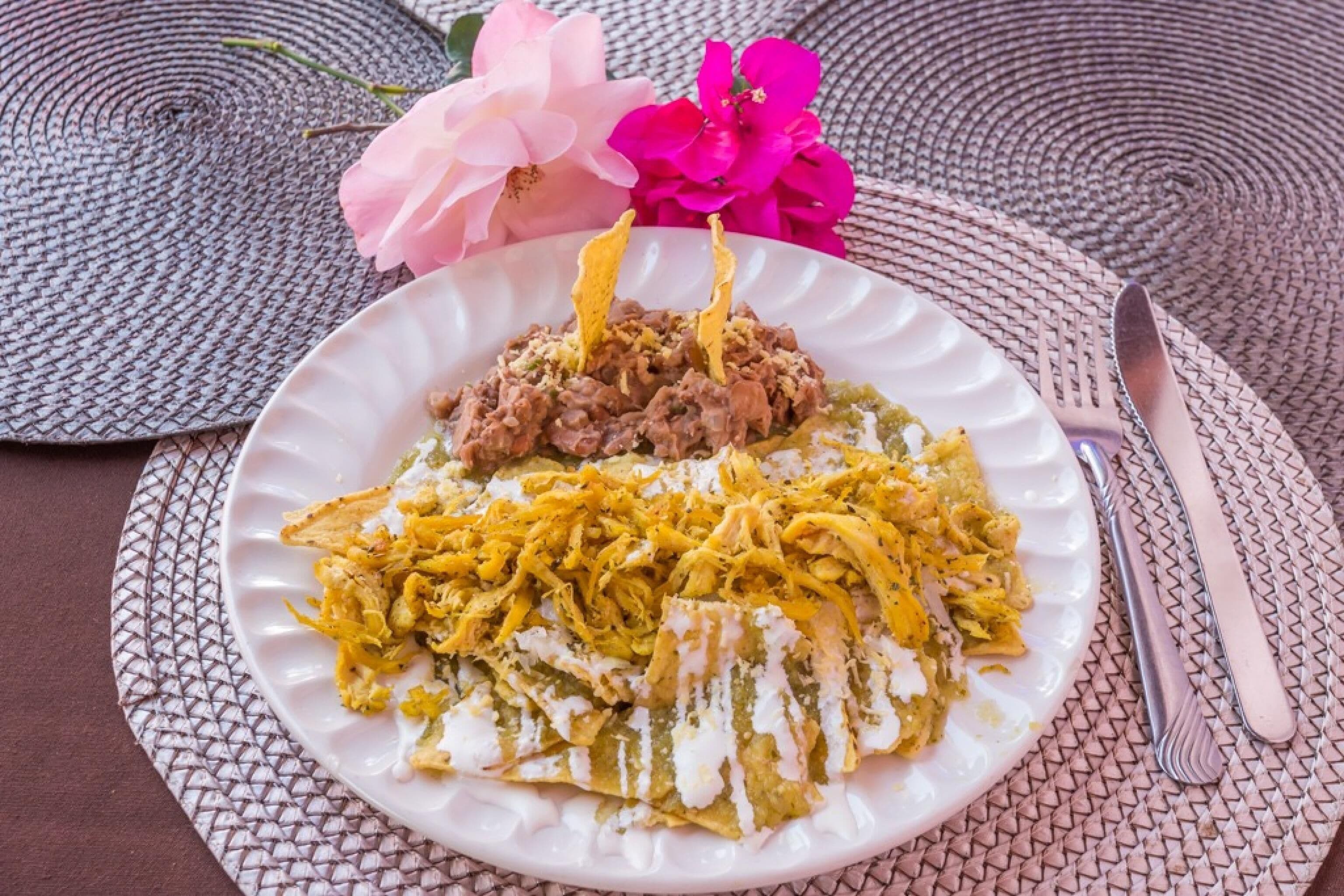 A plate of food with shredded chicken and a green sauce, placed on a woven placemat.
