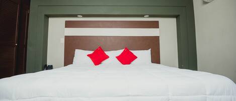 Een net opgemaakt bed met witte lakens en twee rode kussens, een houten hoofdbord en een groene muur.