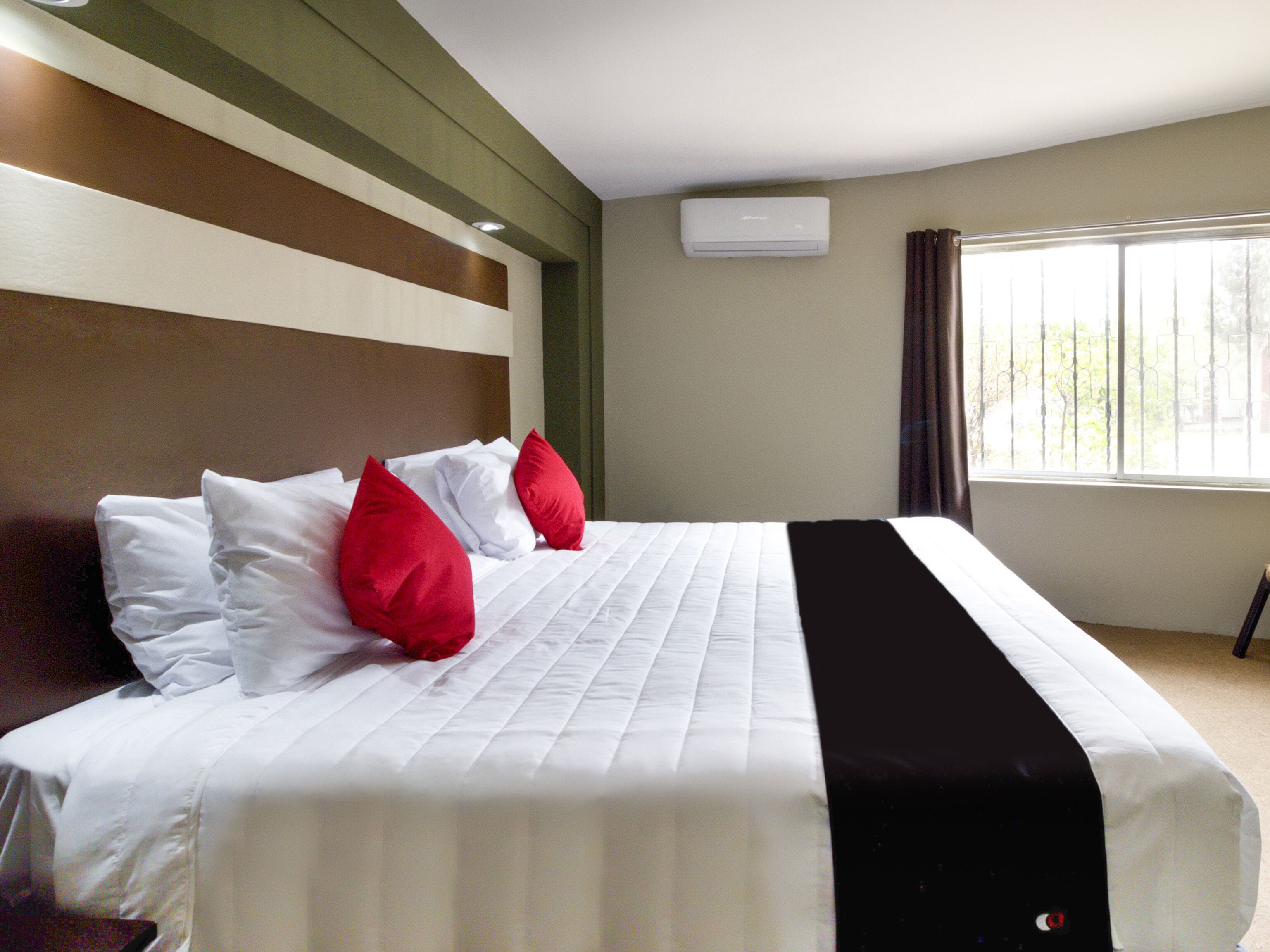 Una habitación de hotel con una cama, un ventanal y un equipo de aire acondicionado.