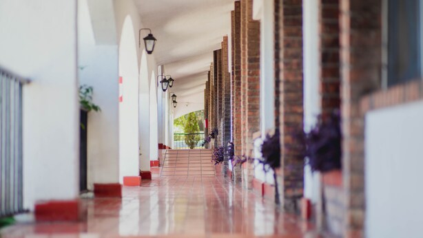A corridor with a tiled floor, brick columns, and a staircase leading to an upper level. - Hotel La Fuente, Saltillo (Saltillo)