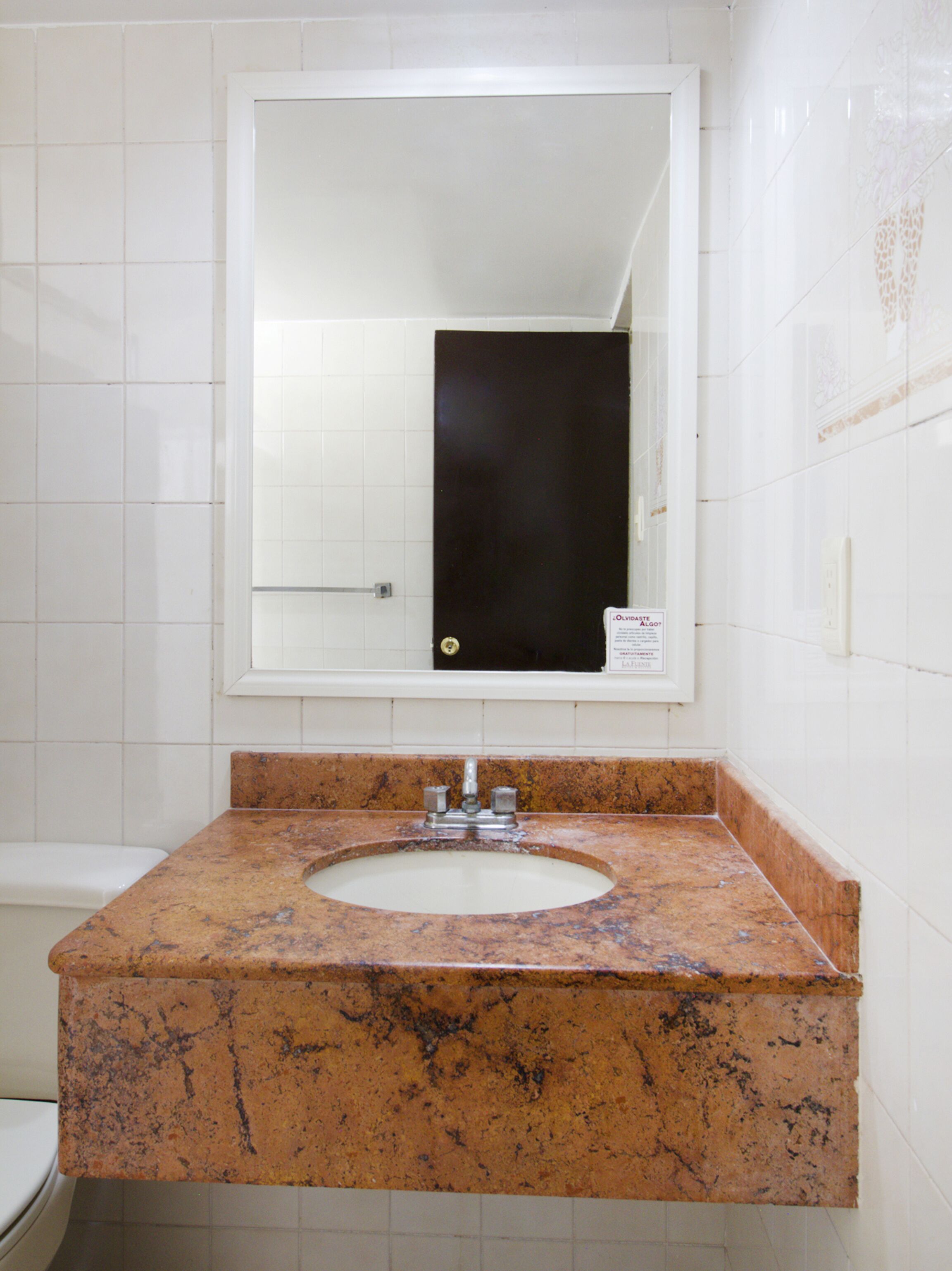 A bathroom with a marble sink, a mirror, and white tiled walls.