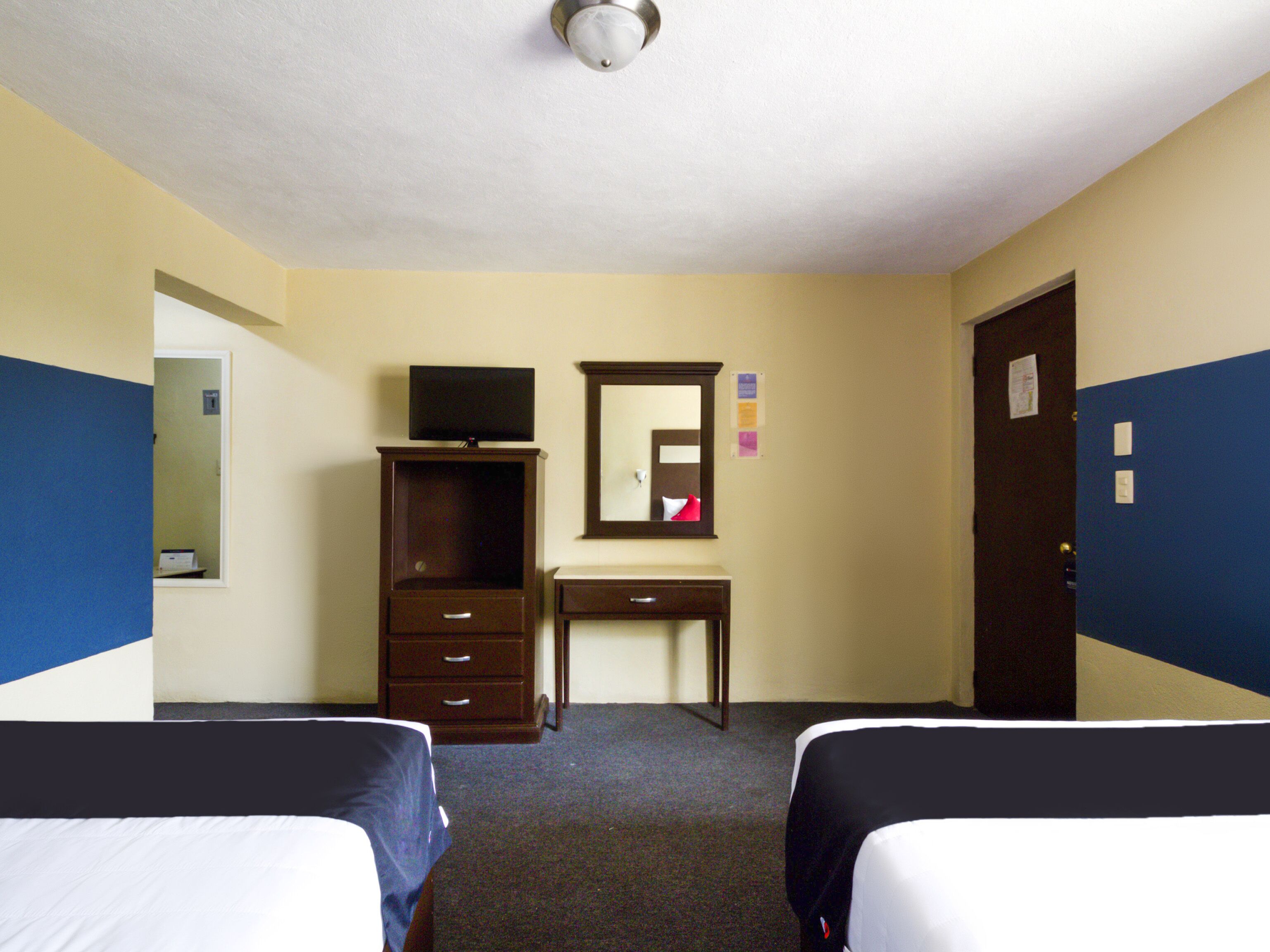 Habitación de hotel con dos camas individuales, un escritorio, un tocador, un televisor y una puerta.