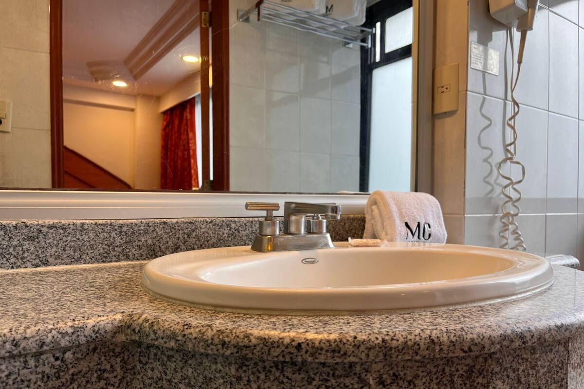 A bathroom with a granite countertop, a white sink, a towel with 'MC' on it, and a mirror above the sink.