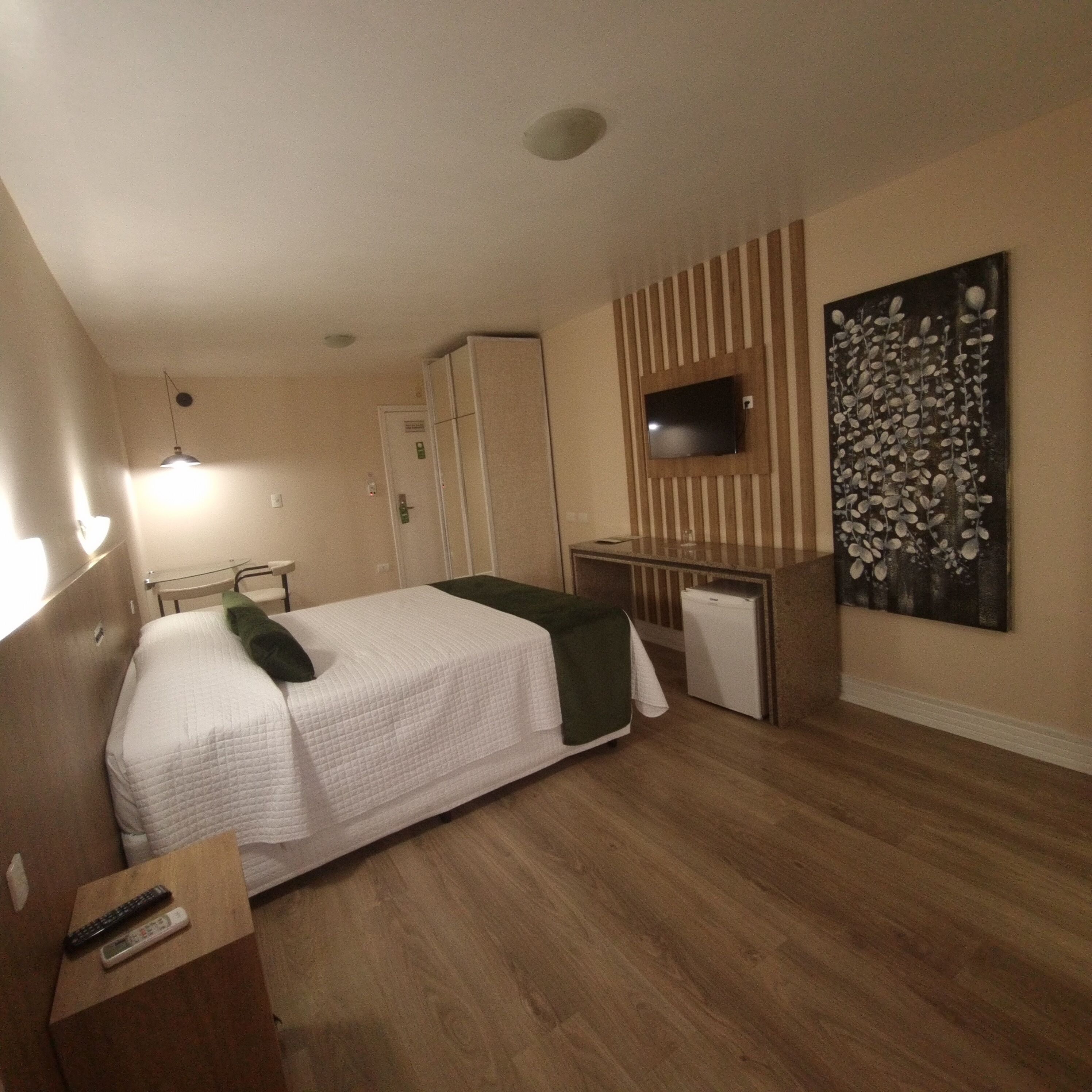 A hotel room with a bed, a desk, a television, and a painting on the wall.
