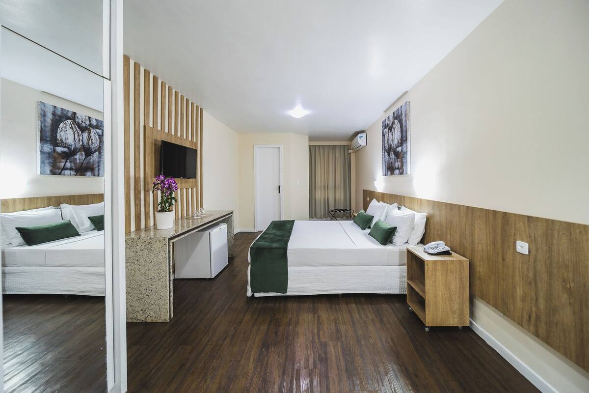 Ein Hotelzimmer mit zwei Betten, einem Schreibtisch, einem Spiegel und Bildern an der Wand.