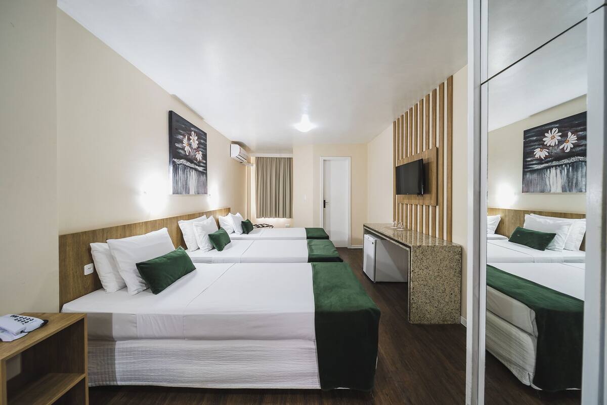 Ein Hotelzimmer mit zwei Betten, einem Schreibtisch, einem Fernseher und einem Spiegel.