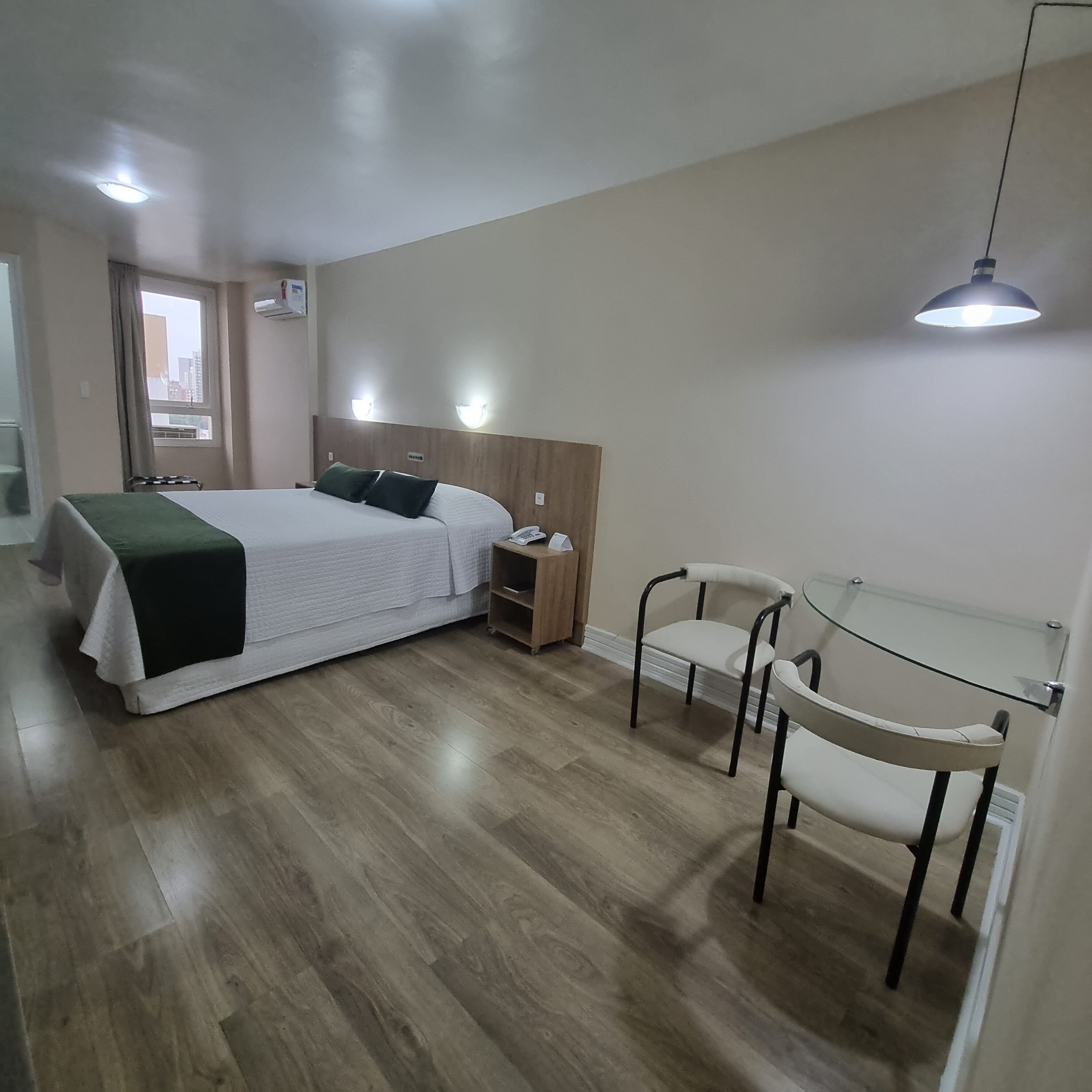 Ein modernes Hotelzimmer mit Bett, Nachttisch, Lampe und einem kleinen Tisch mit Stühlen.