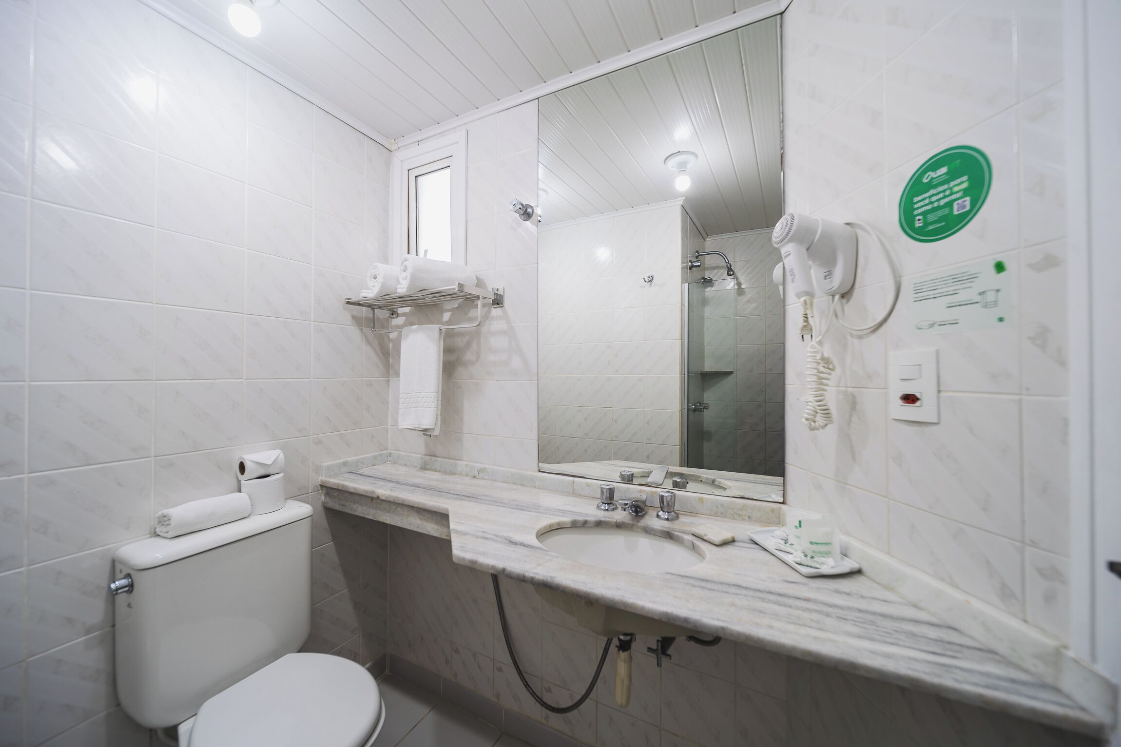 A bathroom with a toilet, sink, and shower. There is a towel rack above the sink and a mirror above the sink.
