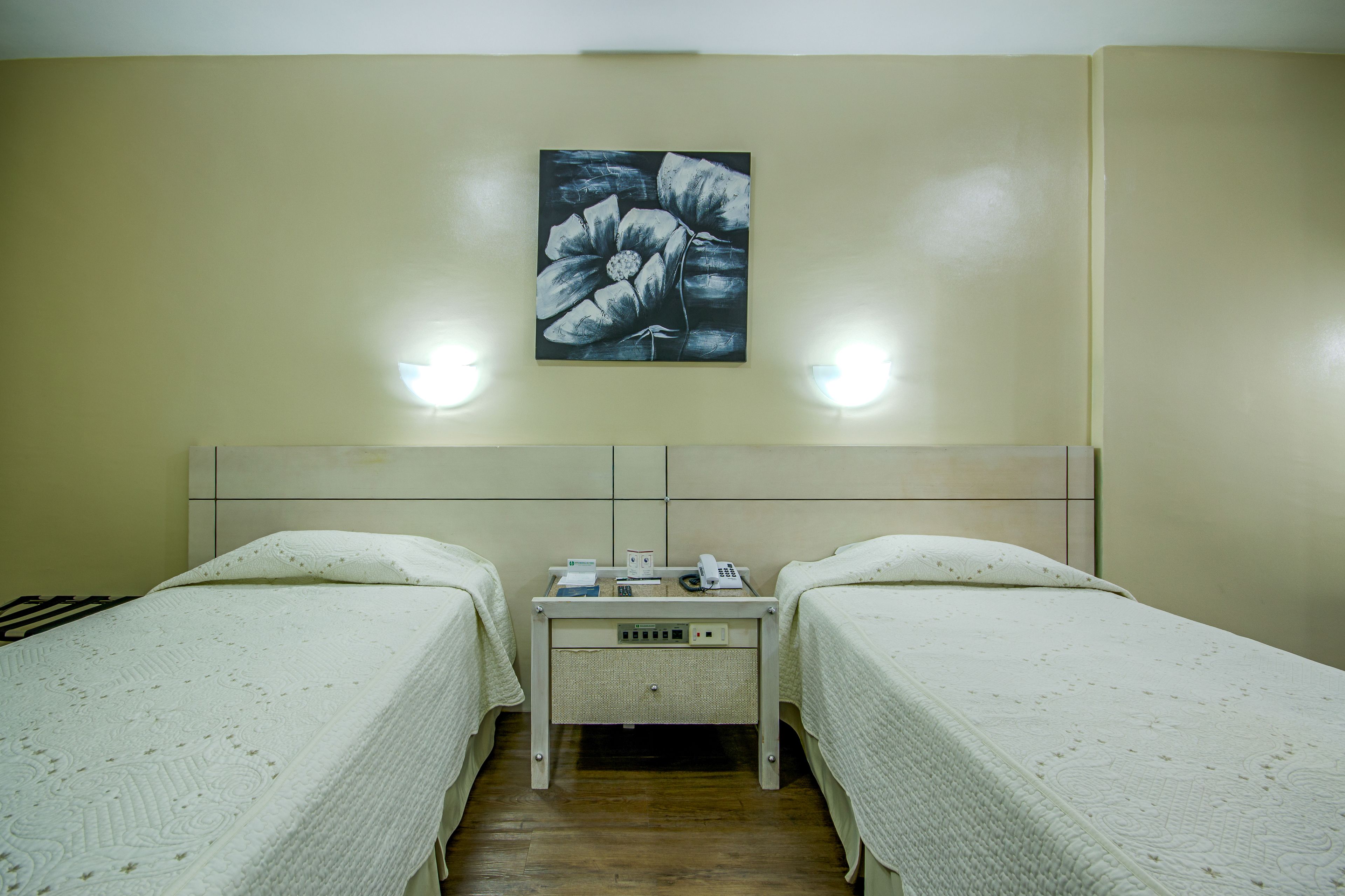 A hotel room with two single beds, a bedside table with a phone and a lamp, and a painting on the wall.