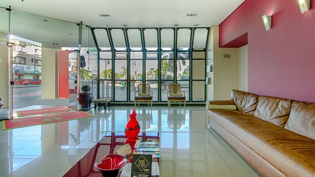 A modern lobby with a leather sofa, a reception desk, and a large window offering a view of the street. - Hotel Nacional Inn Curitiba Torres (Curitiba)