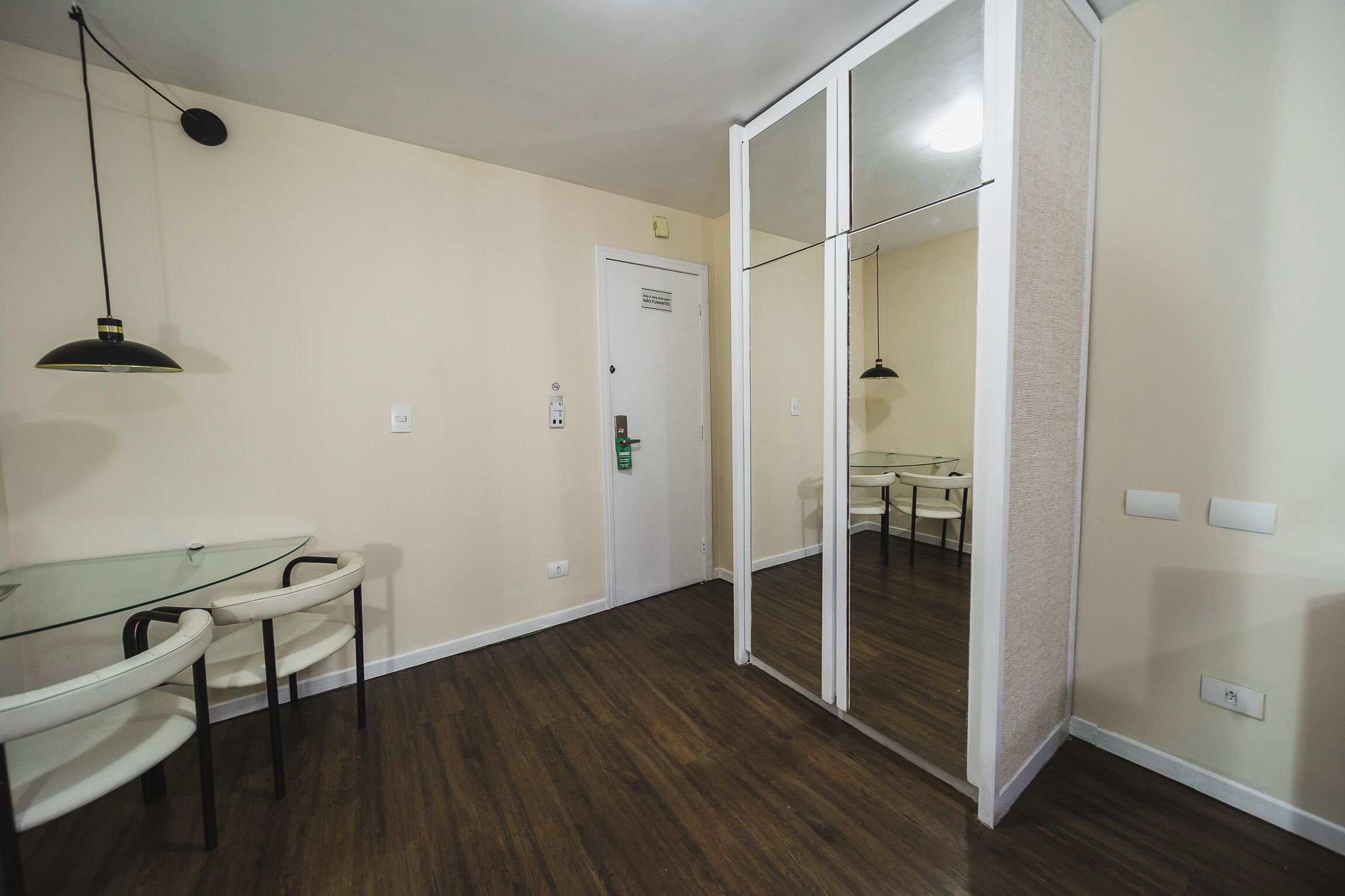 A room with a glass table and chairs, a door with a green lock, and a mirror on the wall.